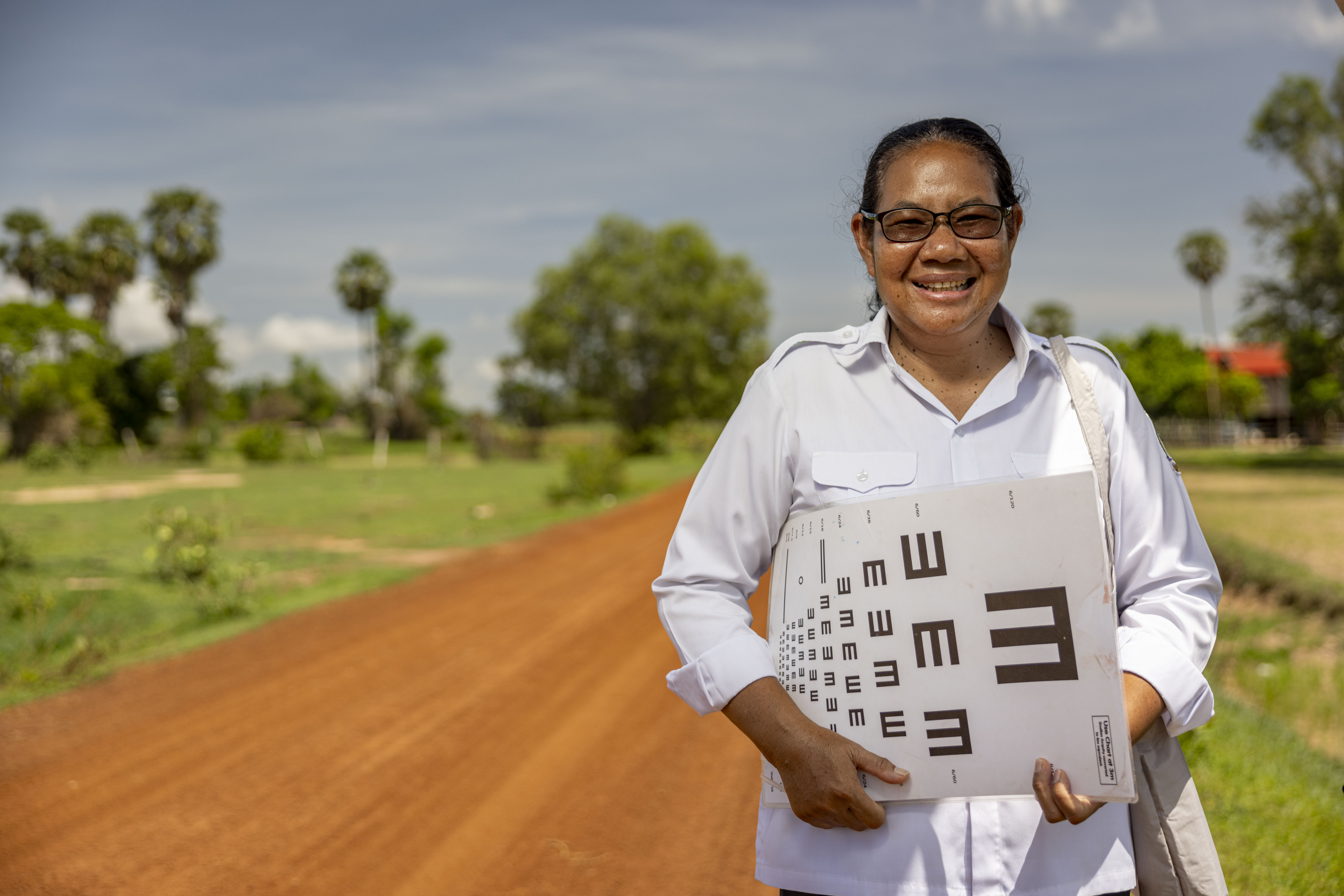 Chhim Sokha standing beside a dirt road in Cambodia while she goes house to house screening people for eye conditions.