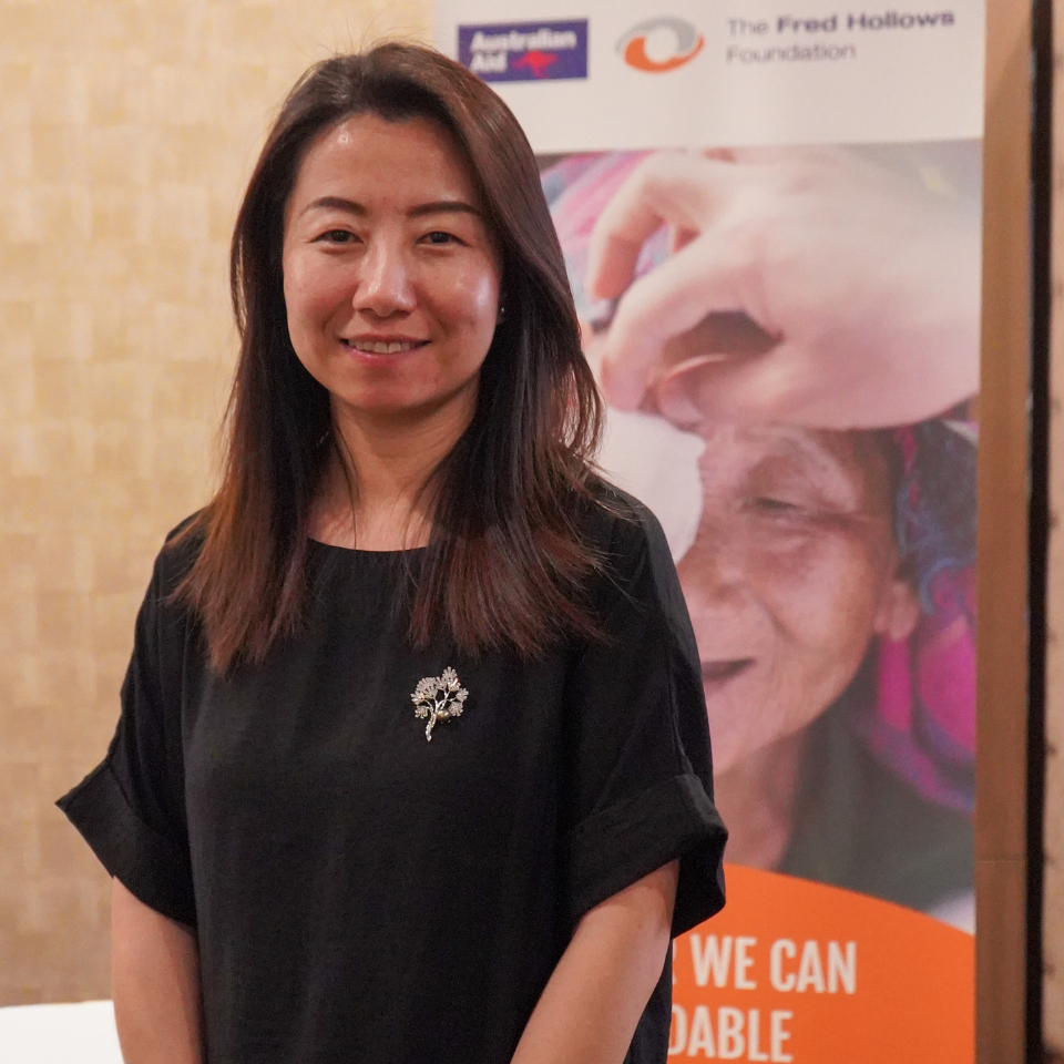 Amanda Huang standing in front of a Fred Hollows Foundation corflute, smiling at the camera. 