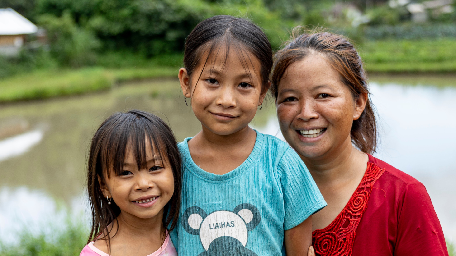 Chansouk at 6 years old, smiling standing next to her younger sister and her mother