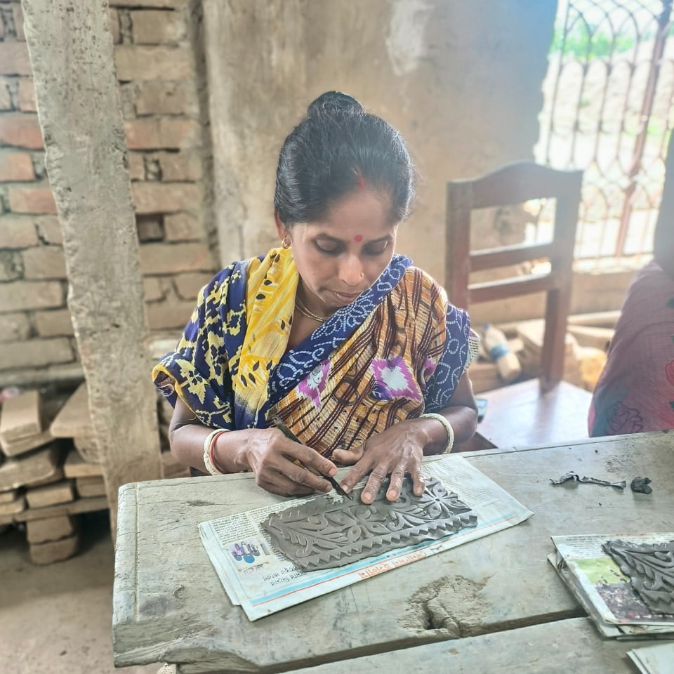 A woman in Bangladesh hand-carving detailed patterns into a piece of clay, focusing on her work in a traditional pottery setting.