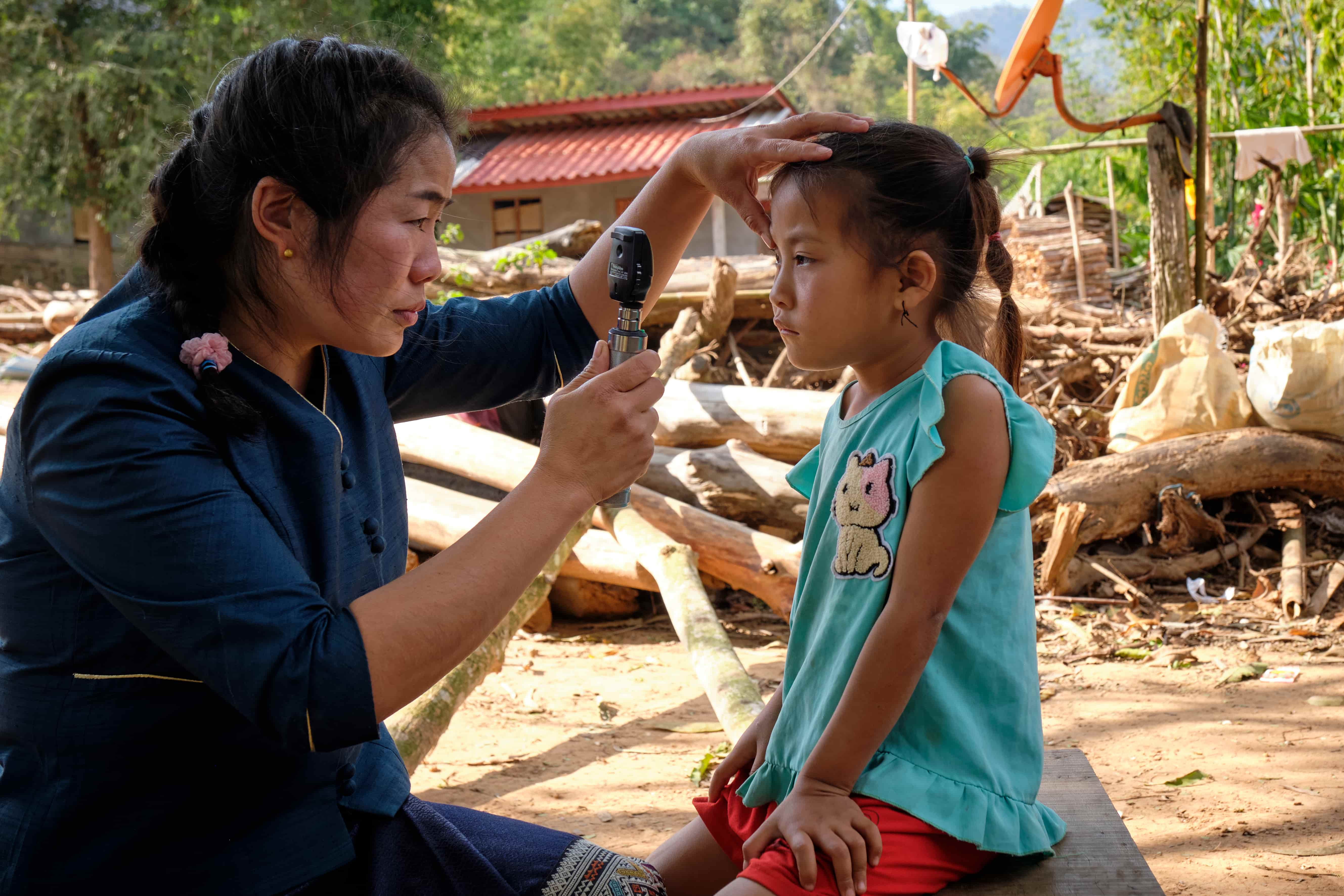 Dr Senglar gently tests six-year-old Chansouk’s vision outside her family’s rural home in Oudomxay, Laos. The young girl has a cataract in her right eye, and Dr Senglar has travelled to her remote village to provide care.