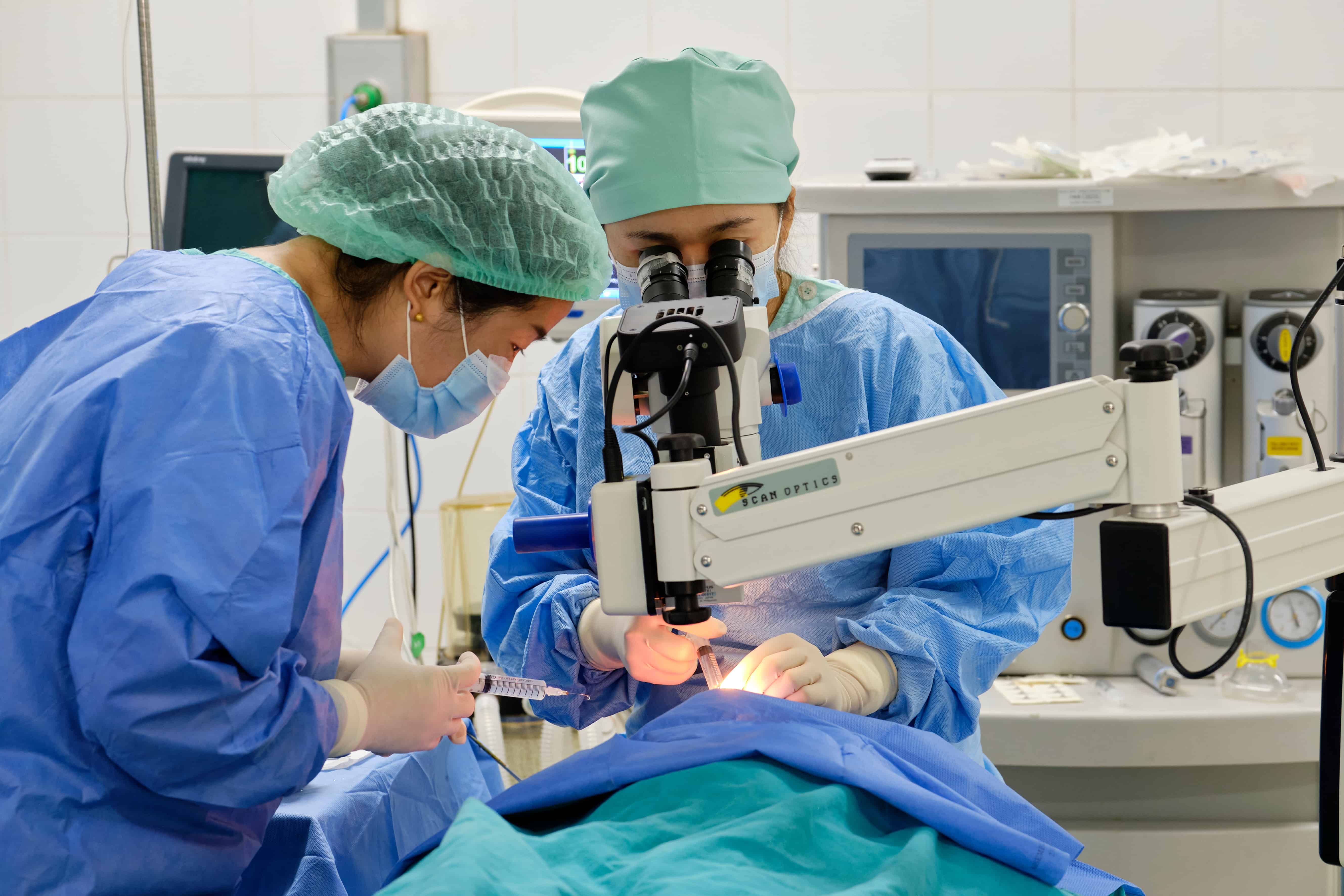 Dr Senglar and visiting surgeon Dr Phatoumphone operate together in a brightly lit theatre at Oudomxay Eye Hospital, performing cataract surgery on six-year-old Chansouk to restore her sight.