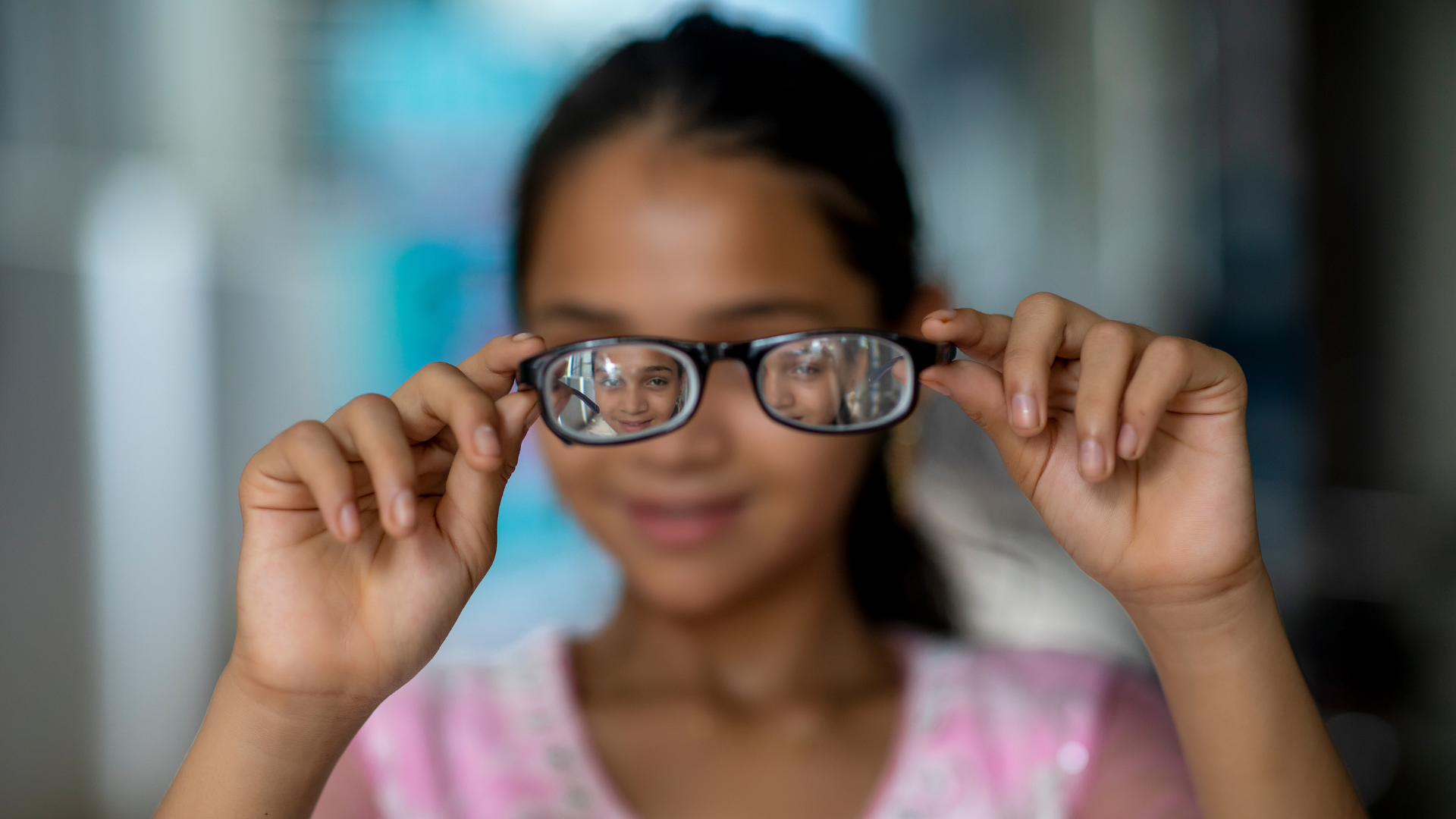 A girl facing the camera holding her glasses in front of her face
