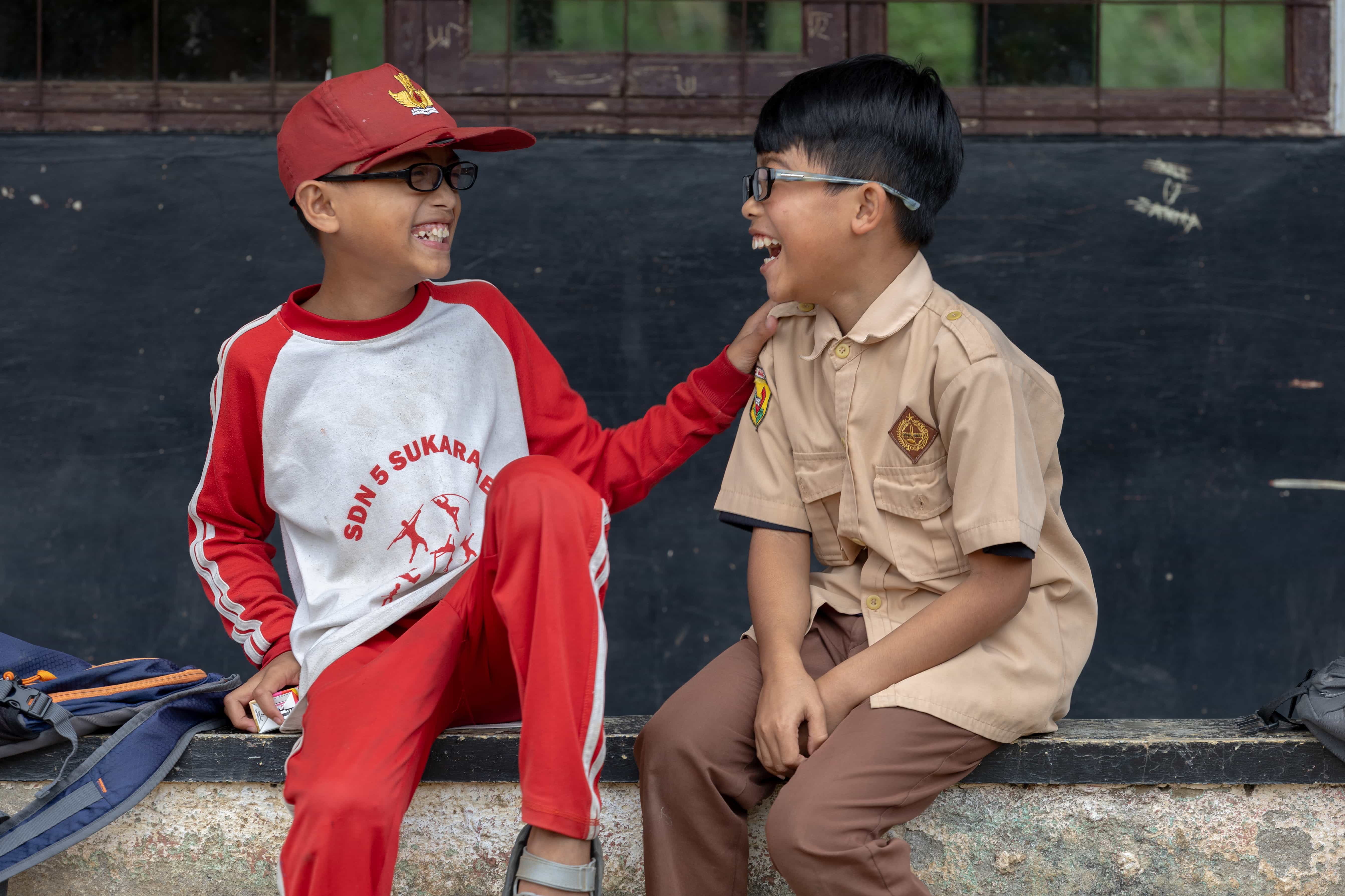 Two boys wearing glasses, smiling at each other