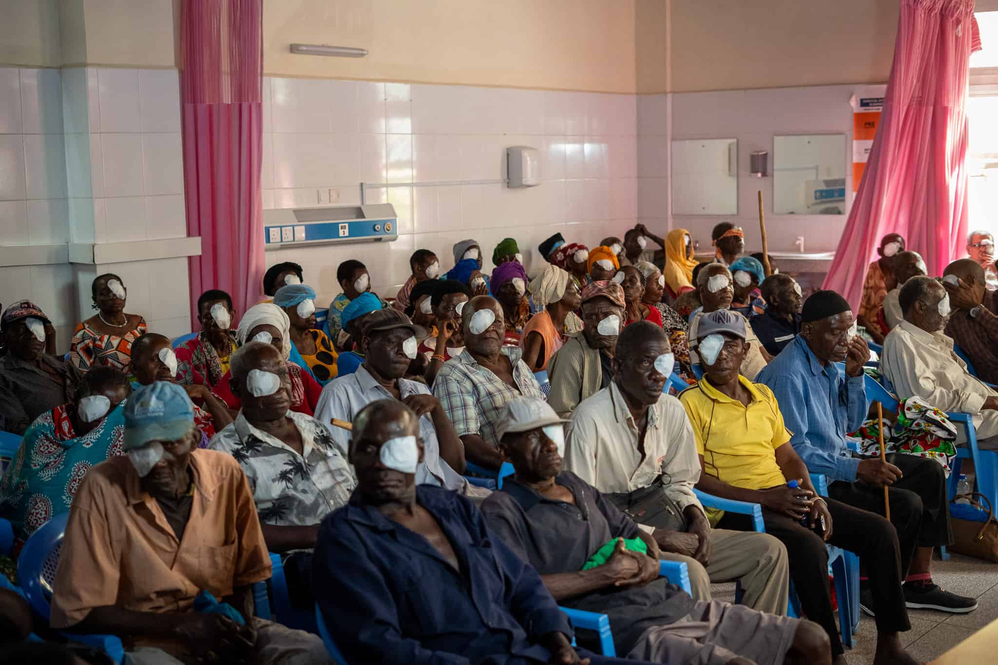 Patients sit together in a hospital waiting area at Kilifi Referral Hospital after having their eye patches removed following surgery.