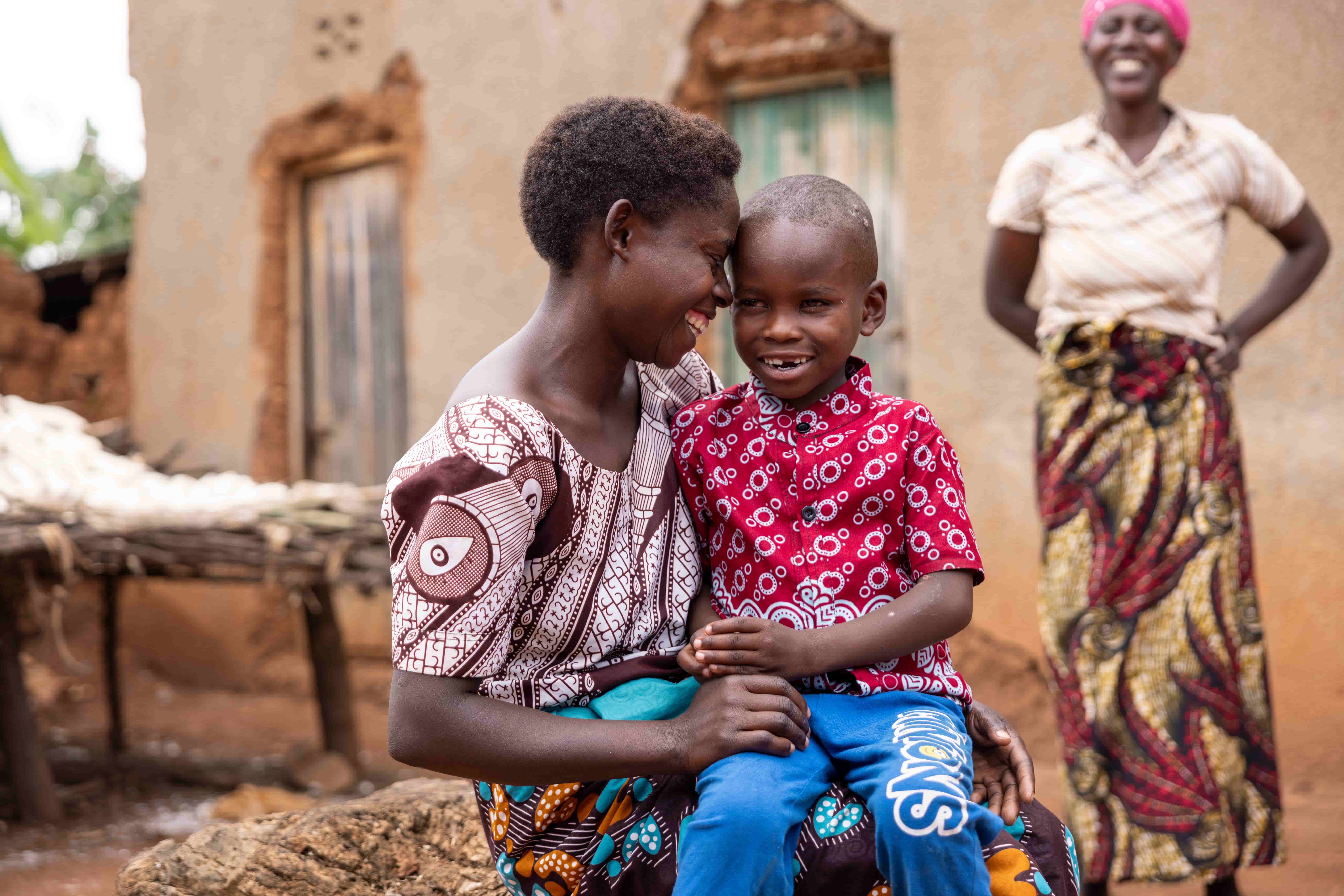 Blaise sits on his mother Redempta&rsquo;s lap outside their home, both beaming with happiness after his sight was restored.