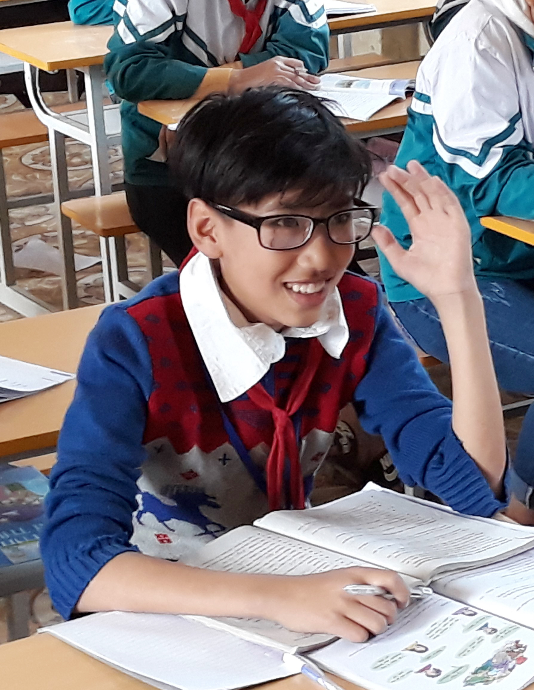 Nghia at his school desk, smiling with his new glasses on
