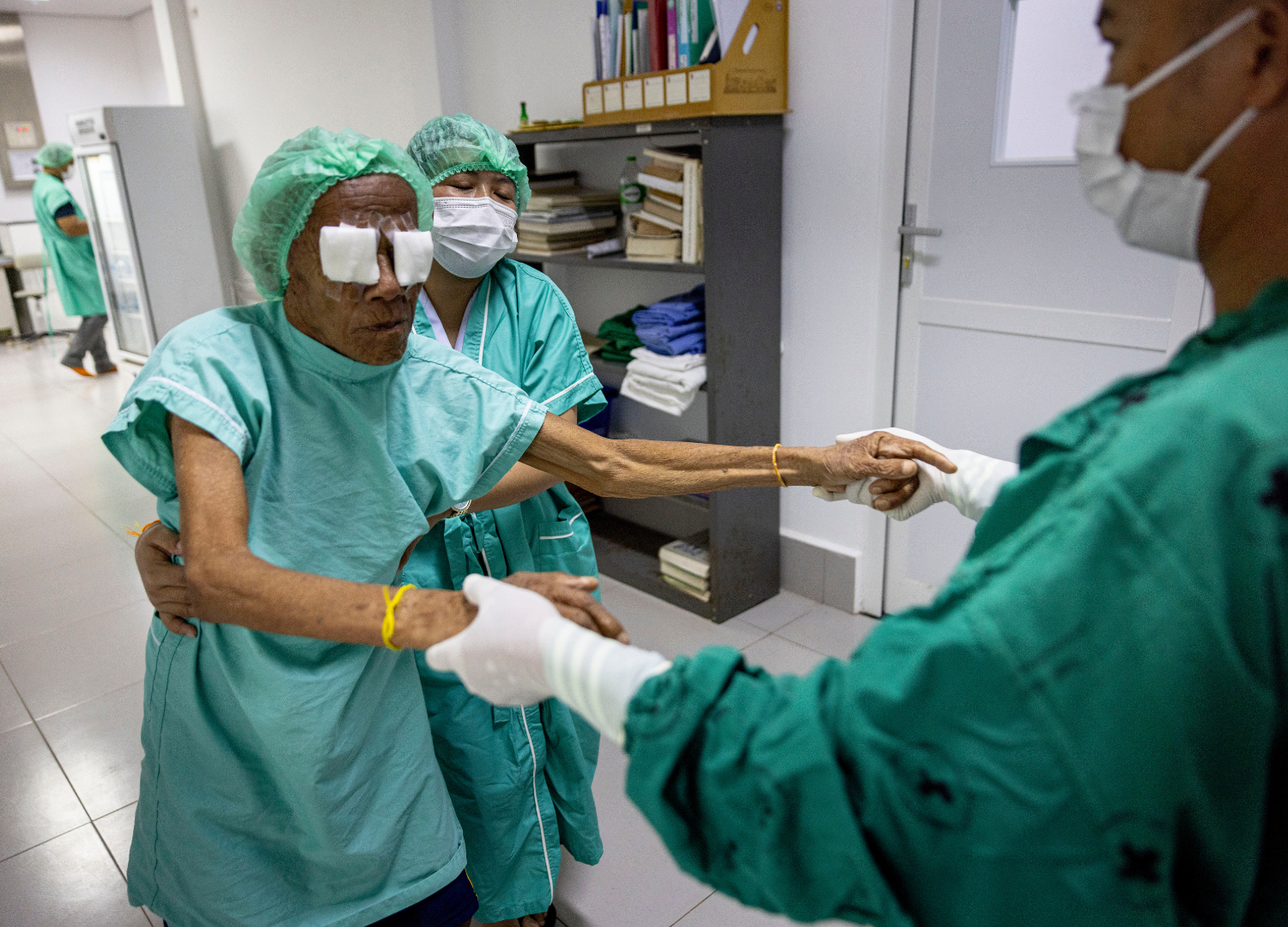 Thoung with his scrubs and eye patches on, being led out of surgery by Dr Visay.