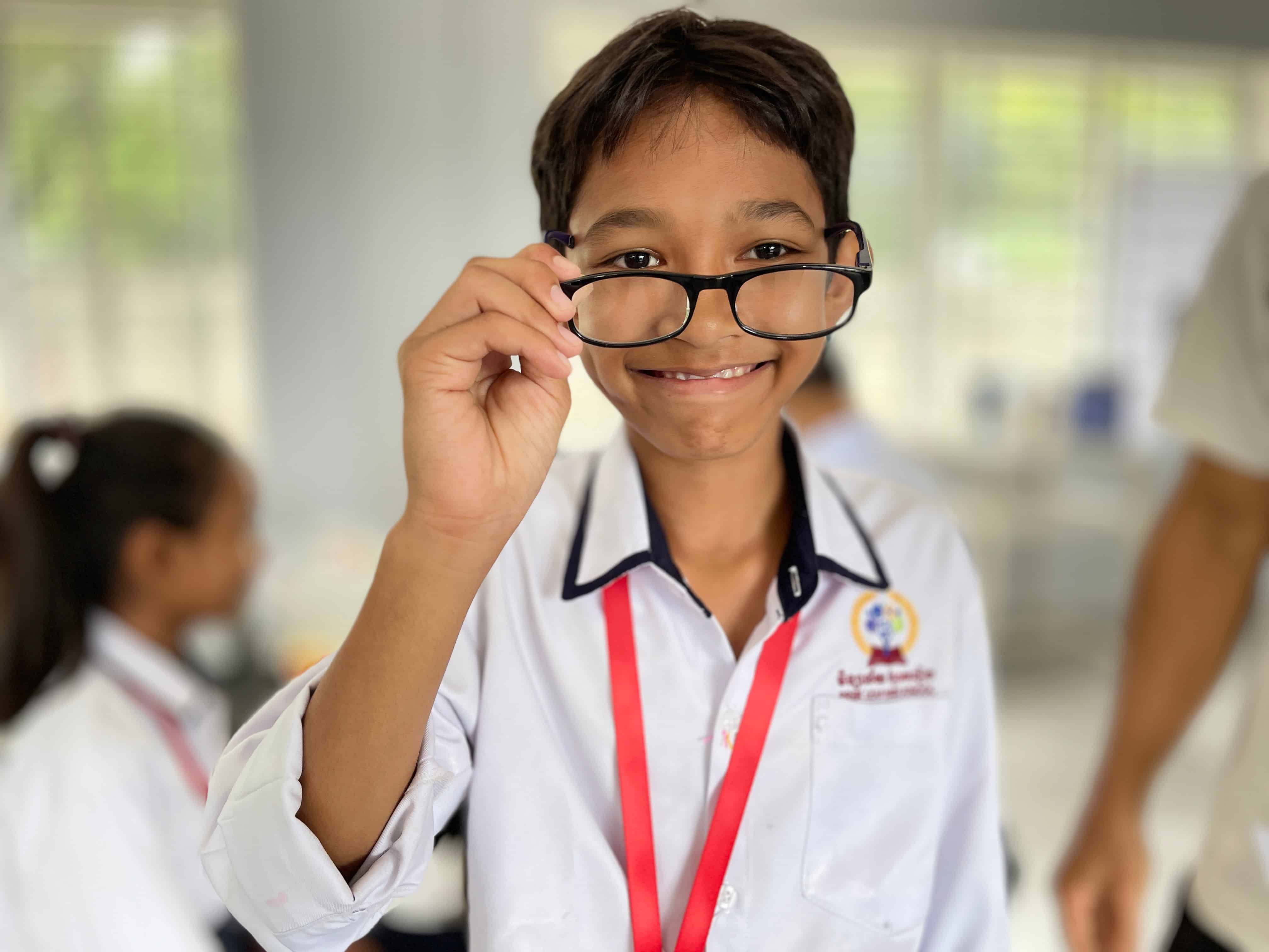A student wearing new glasses after a vision screening at Preak Leap High School, helping him see clearly and continue learning.