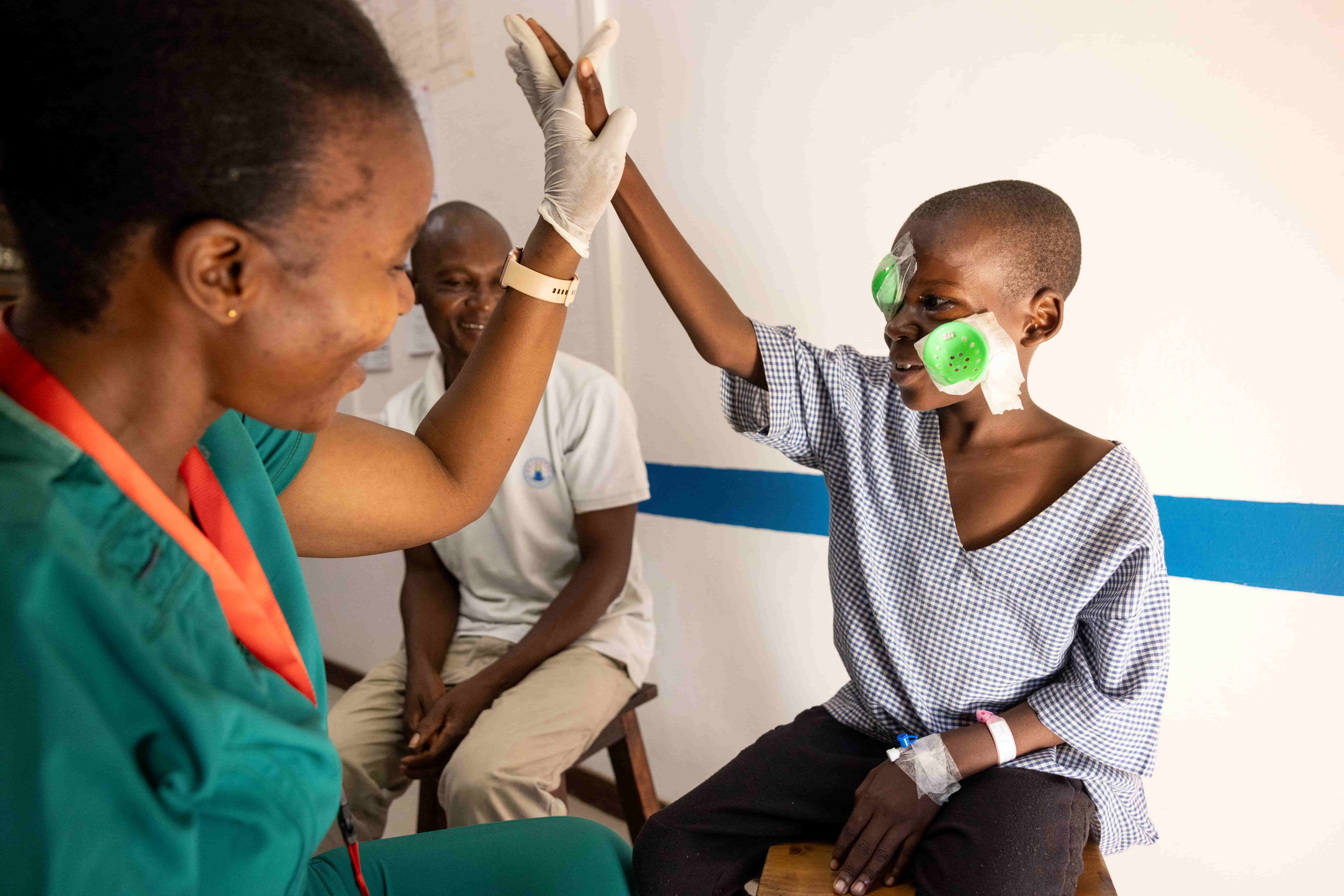 Samson, a young boy from Mazeras village, Kenya, high-fives a healthcare worker after having his eye patch removed following cataract surgery.