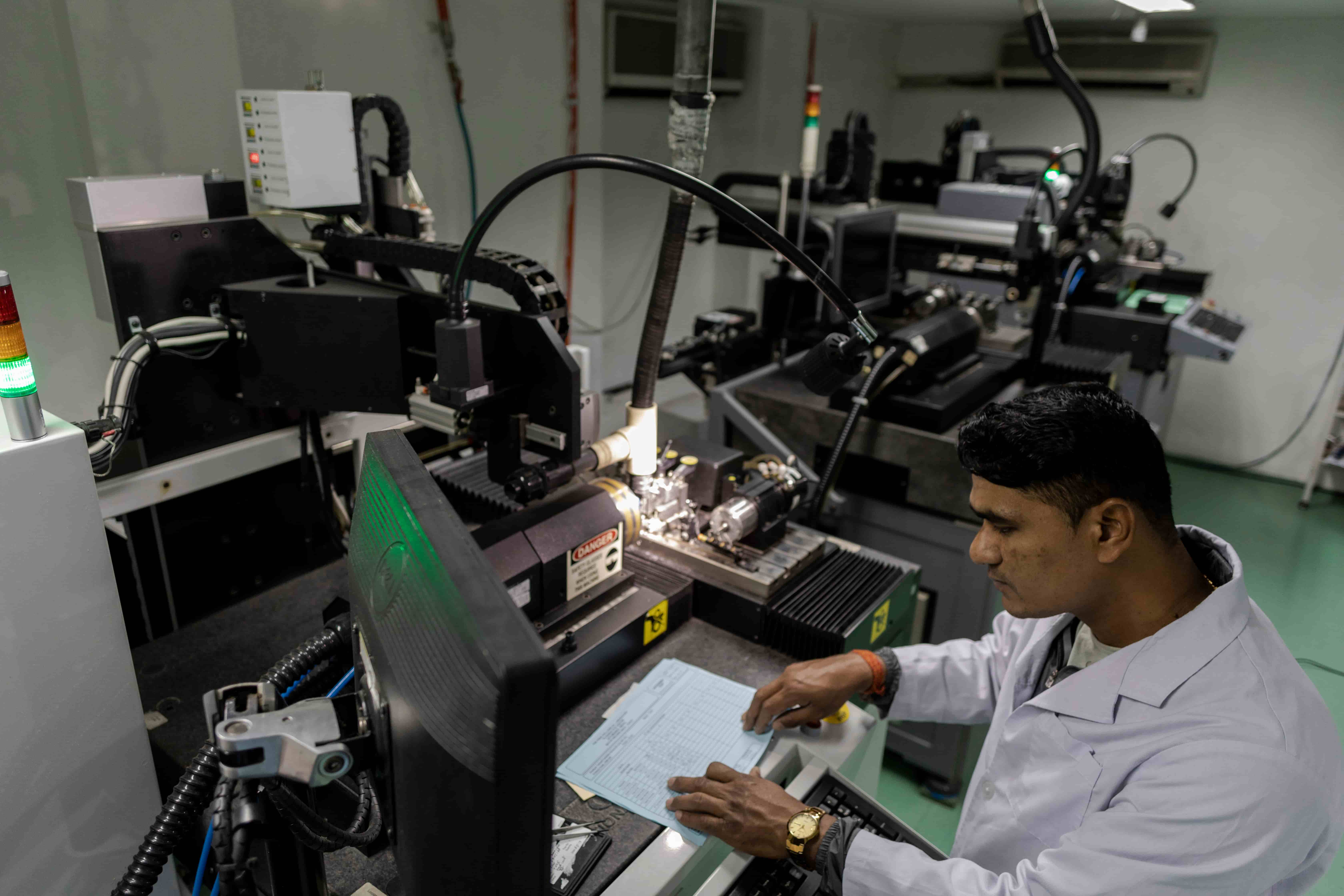 A man seated at a workstation inside the Kathmandu Intraocular Lens Laboratory, surrounded by lab equipment and machinery used to manufacture eye lenses