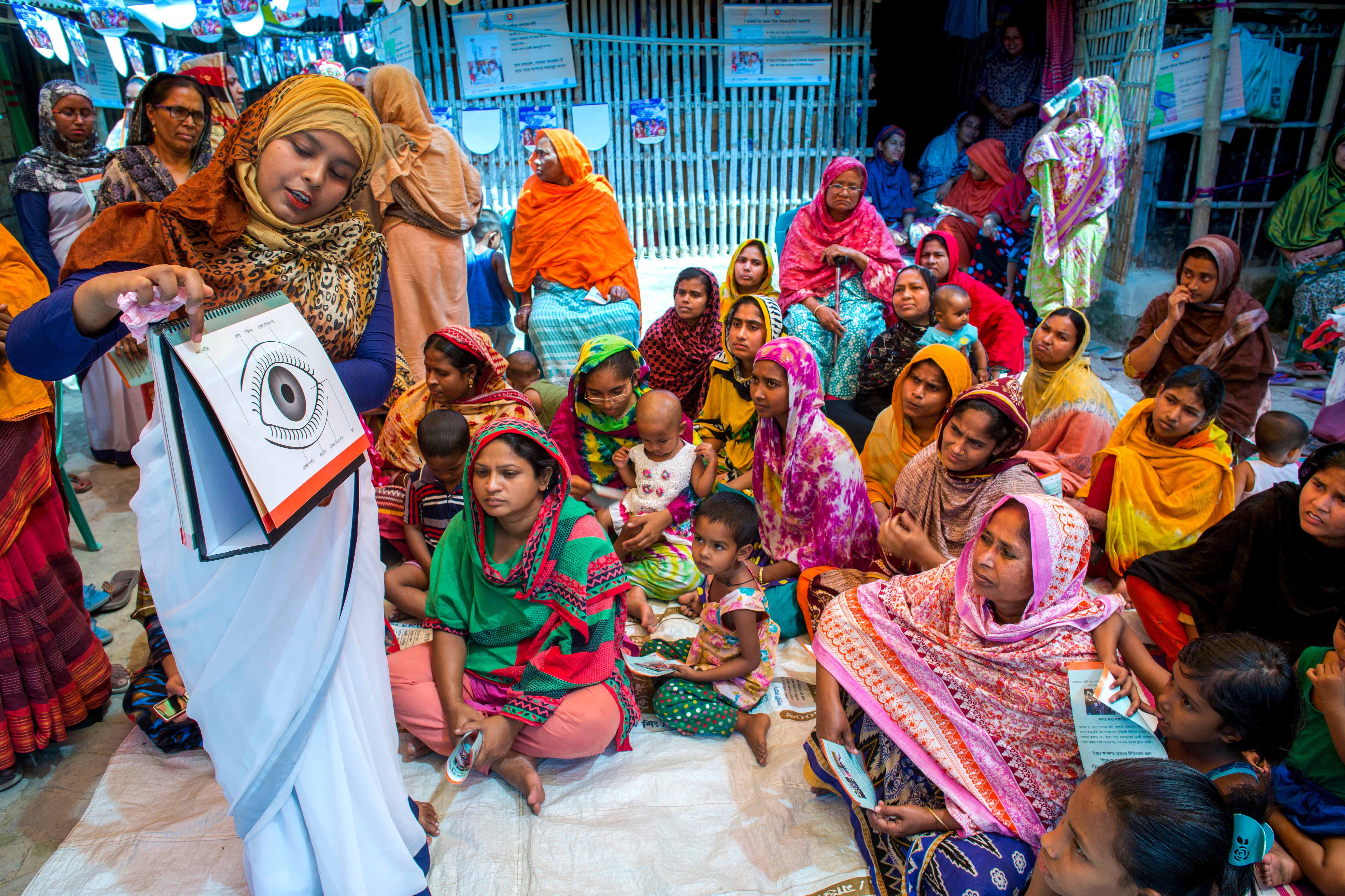 A maternal child health worker gives a presentation to mothers and children about eye health.