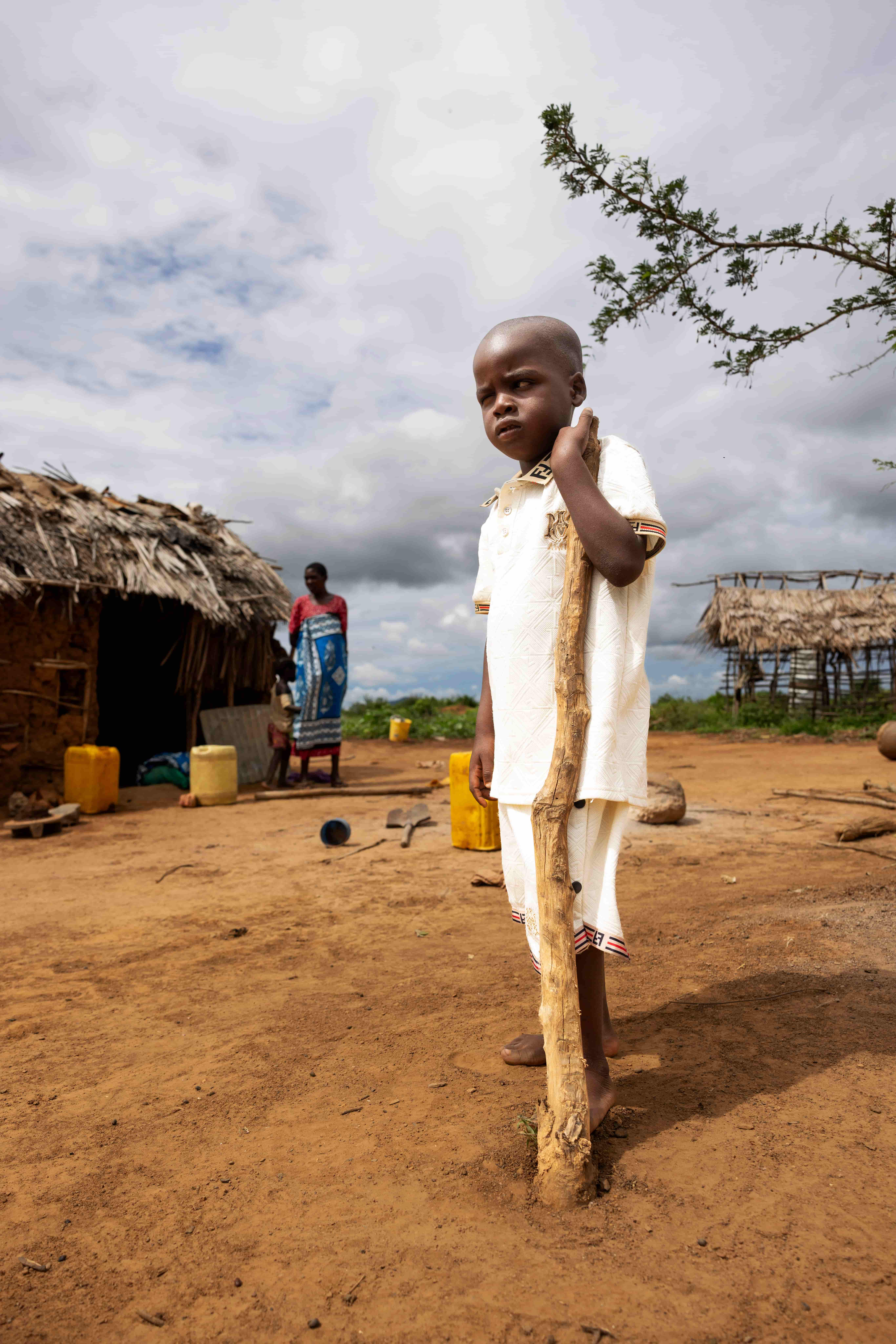 Jira holding onto a large stick, standing outside of his home in remote Kenya.