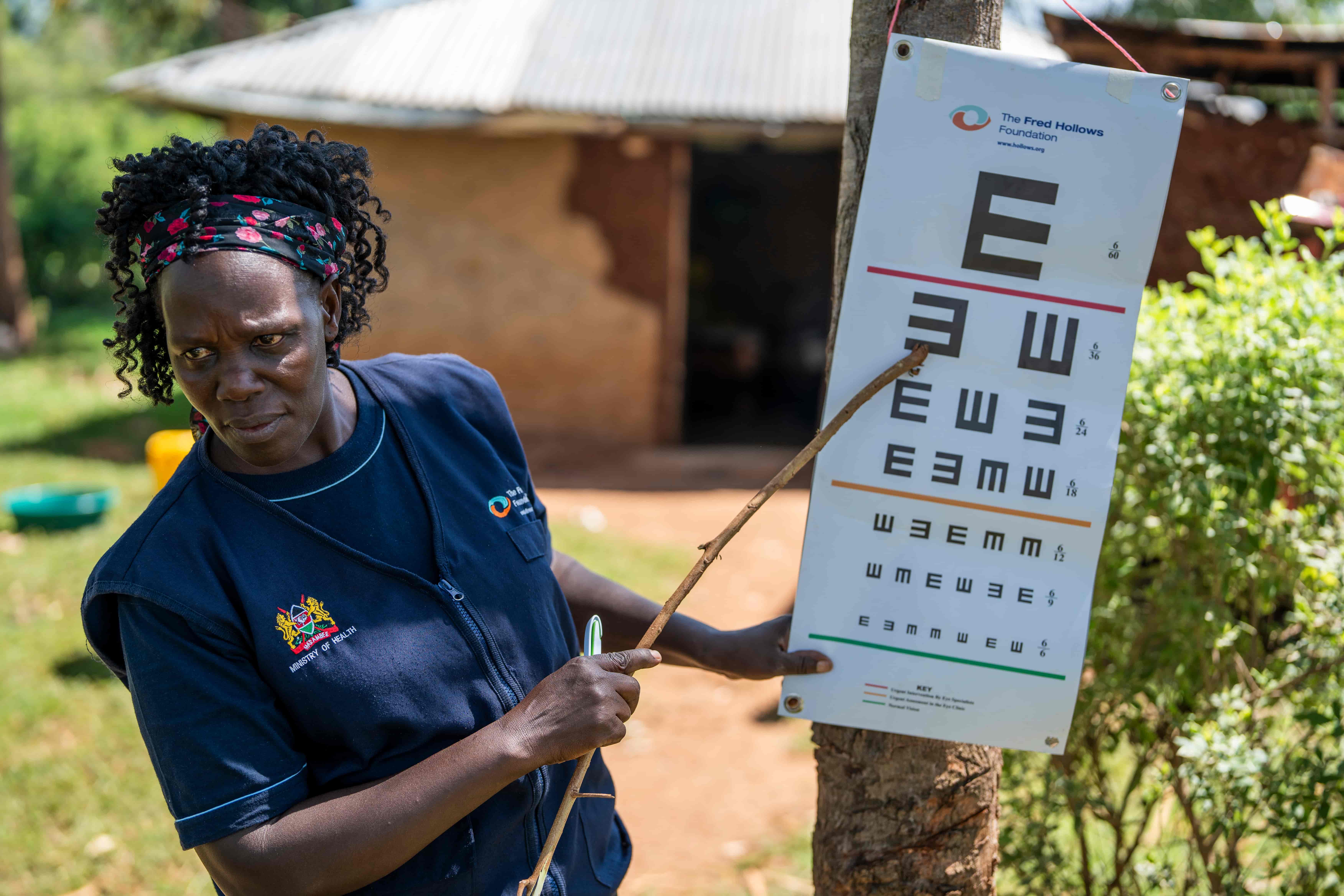 A health worker in Kenya holding up an eye test, pointing at a letter on the test.
