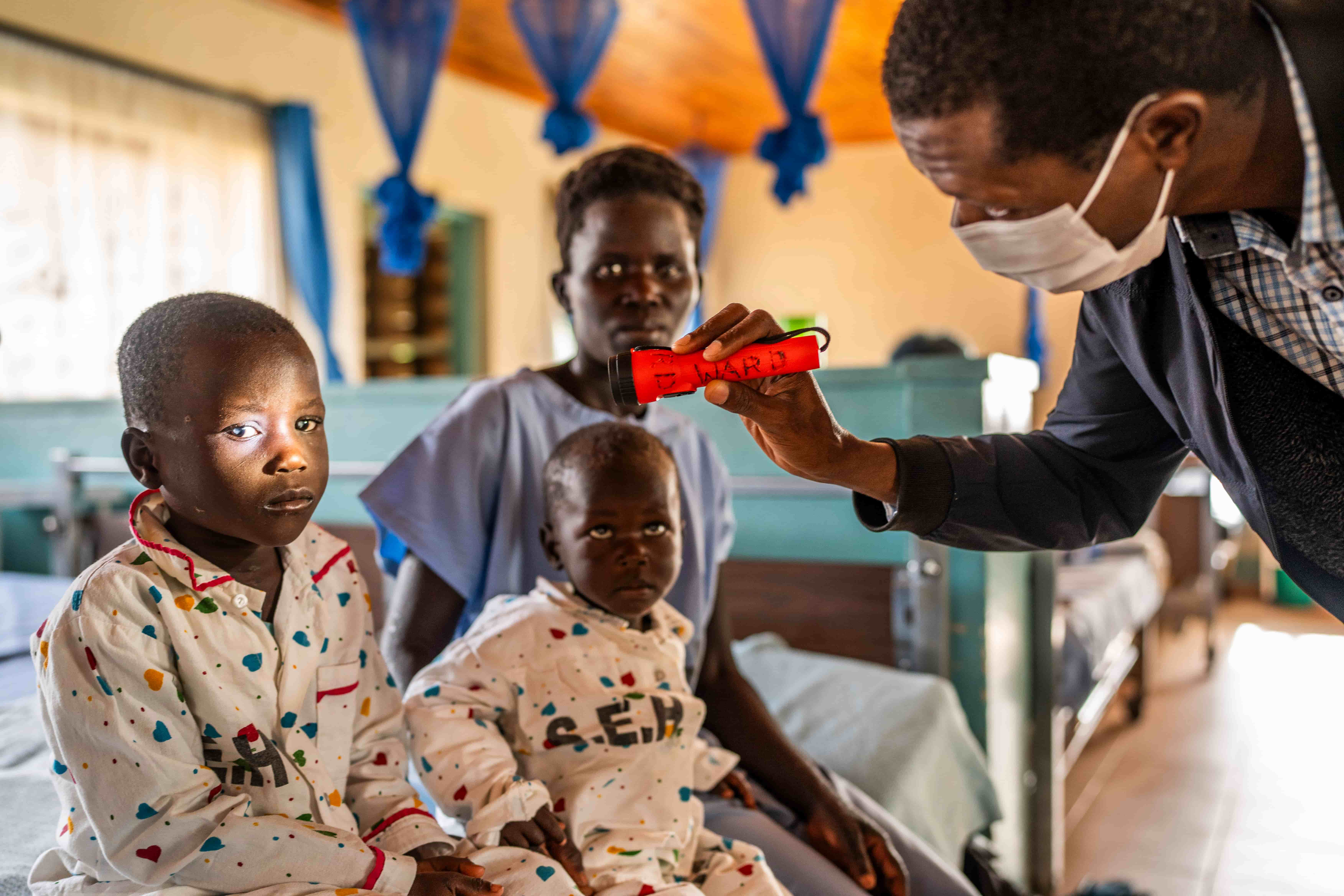 Eveline, Ruth and Vincent in hospital. A health worker is examining their eyes with a torch before surgery.