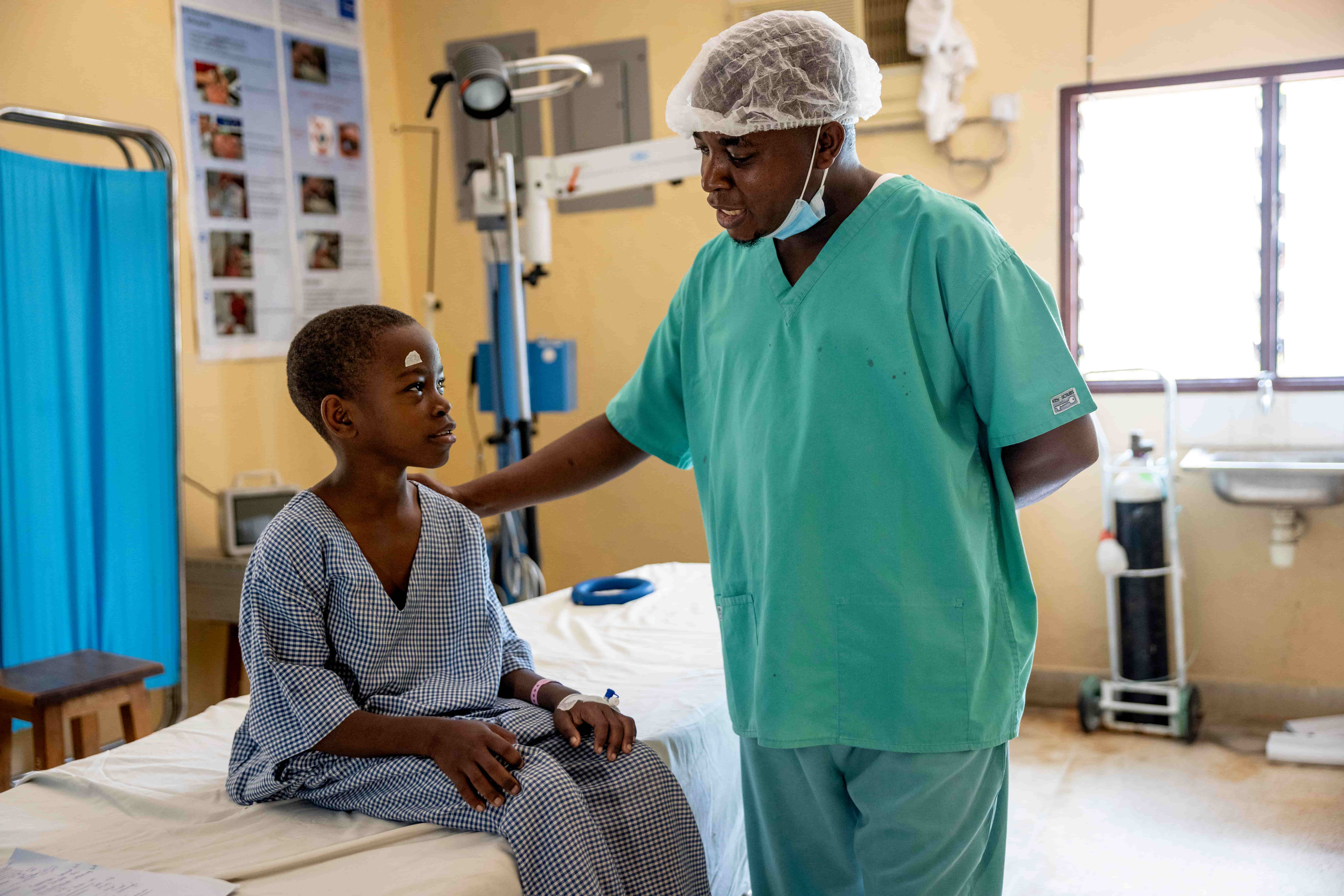 Gift, 11, sits on a hospital bed as a surgeon explains his upcoming cataract surgery in Kilifi, Kenya