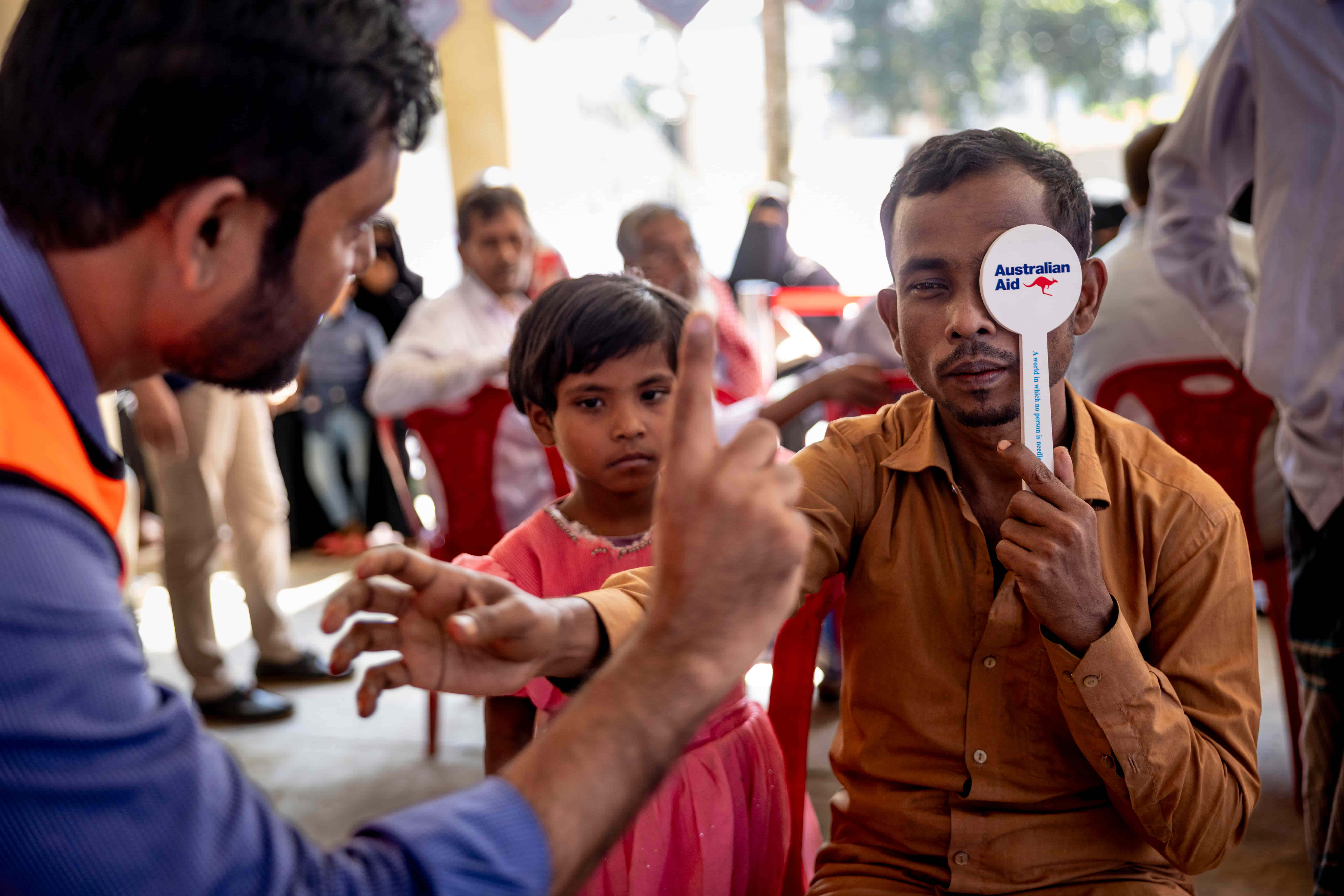 During an eye screening in Cox’s Bazar, Obaidul reaches toward a clinician as cataract limits his vision.