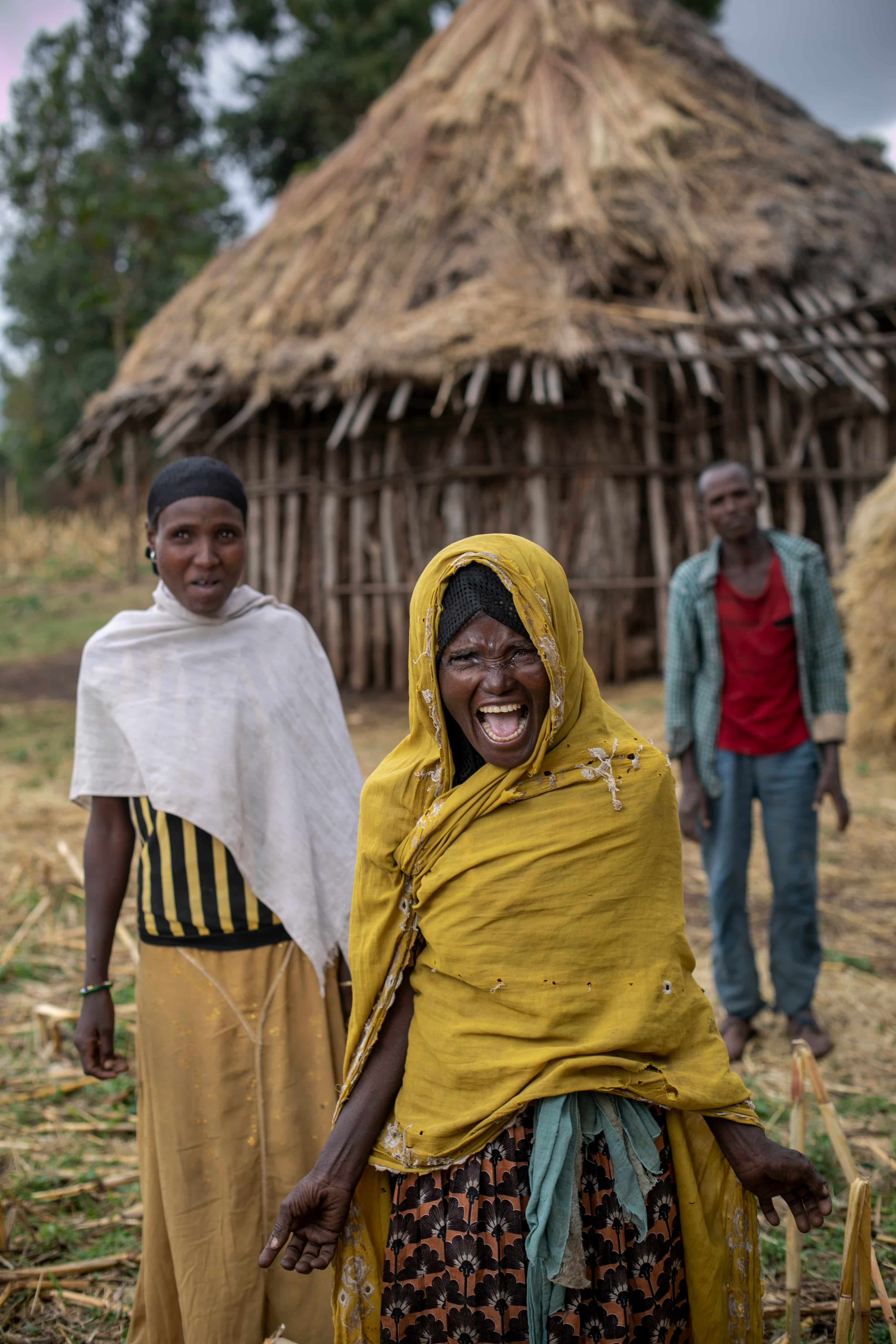 Hawiti wearing a yellow scarf, smiling in front of her mud brick home