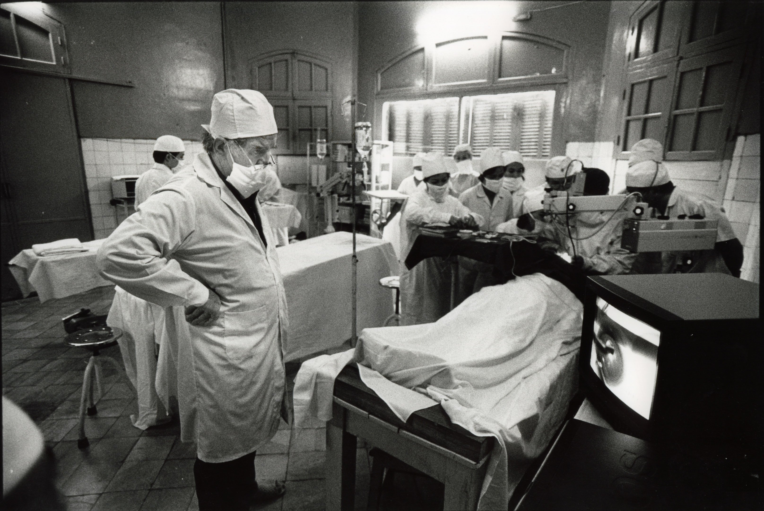  Professor Fred Hollows watches the screen donated to the Institute of Ophthalmology as Vietnamese eye surgeons watch Dr Sanduk Ruit perform a cataract surgery in Hanoi in 1992.