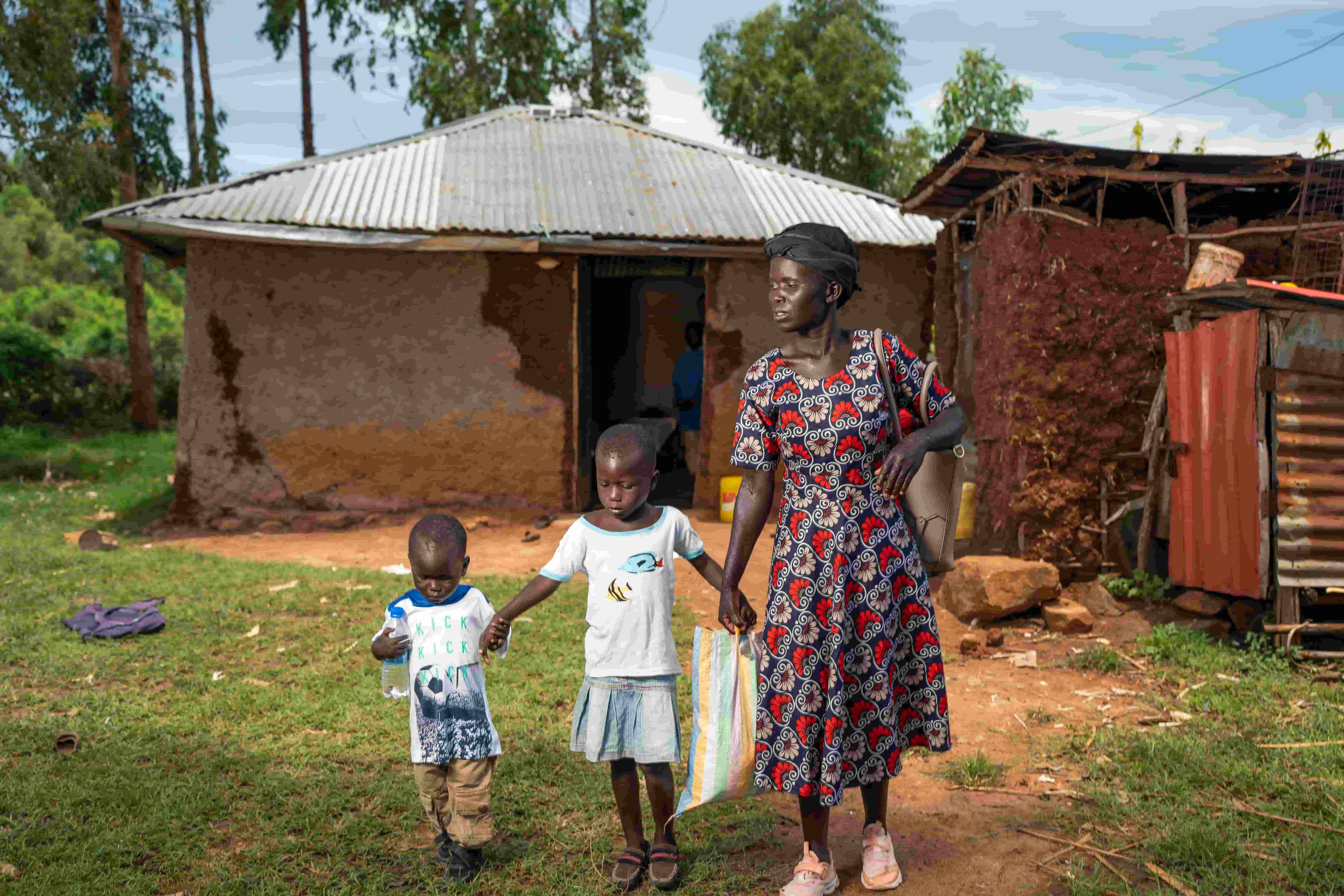 Eveline and her children outside their family home, shortly after accessing eye health services supported by The Fred Hollows Foundation.