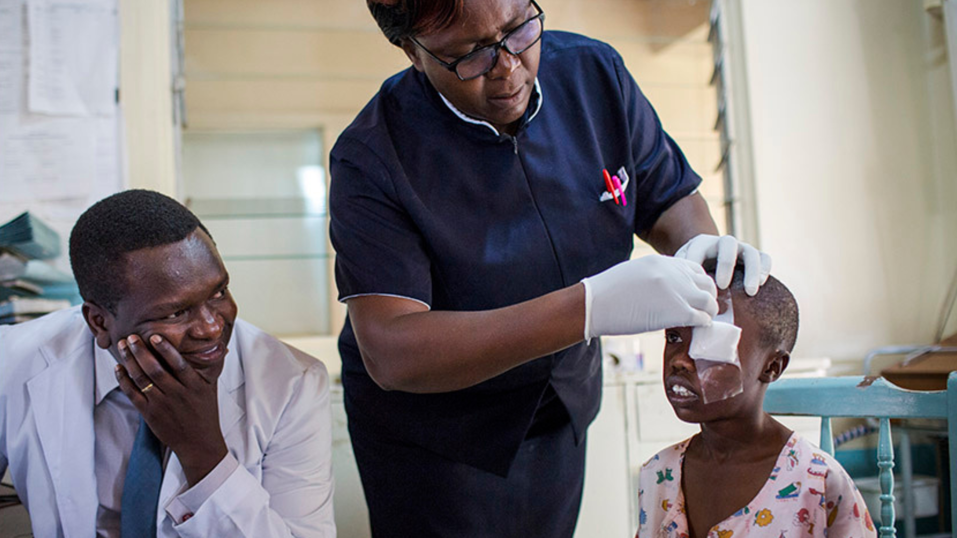A health worker taking off a child's eye patch while the doctor looks on