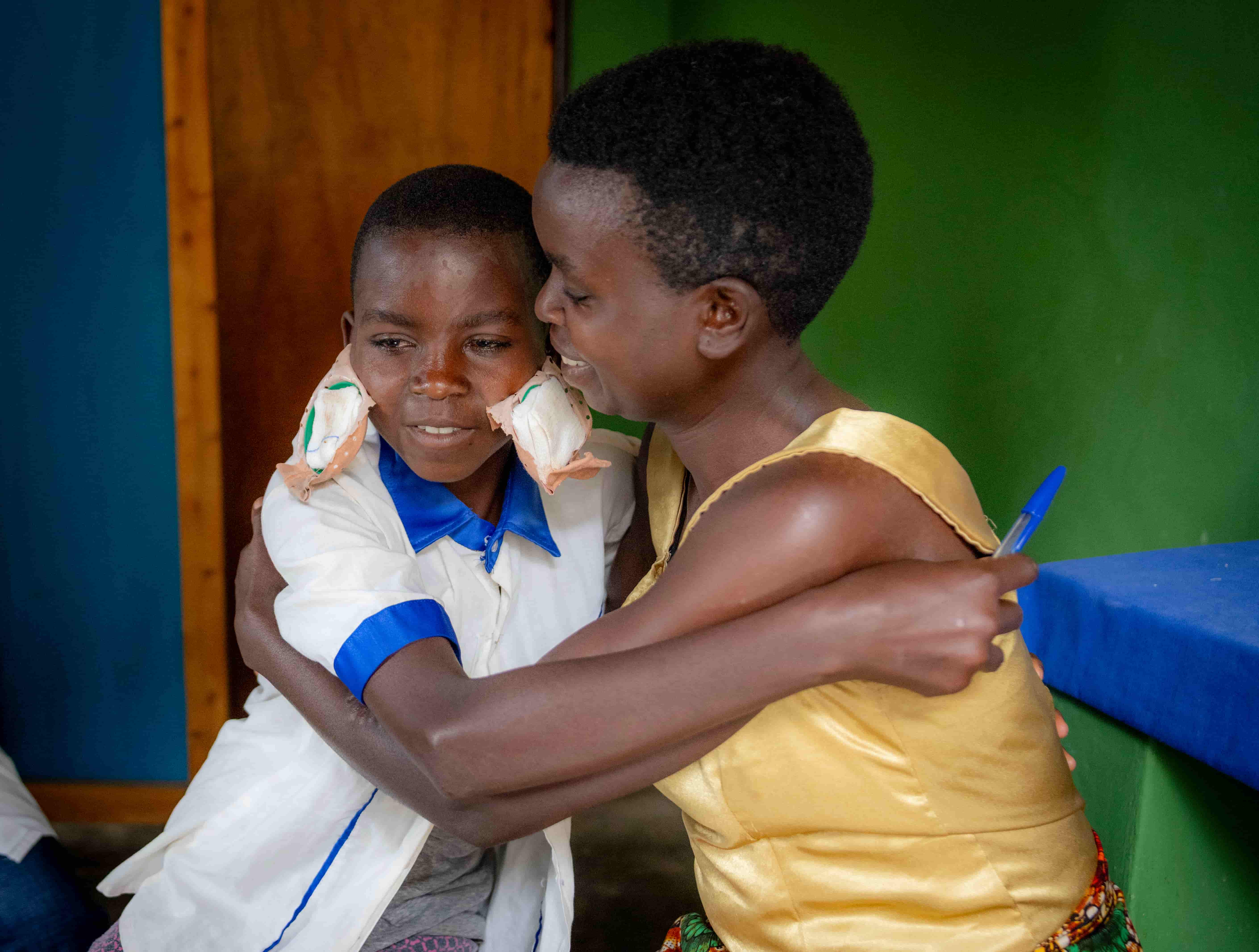 Valentine, 12, embraces her mother Claudine at home after her eye patches are removed following cataract surgery. She is smiling as she regains her vision and confidence.