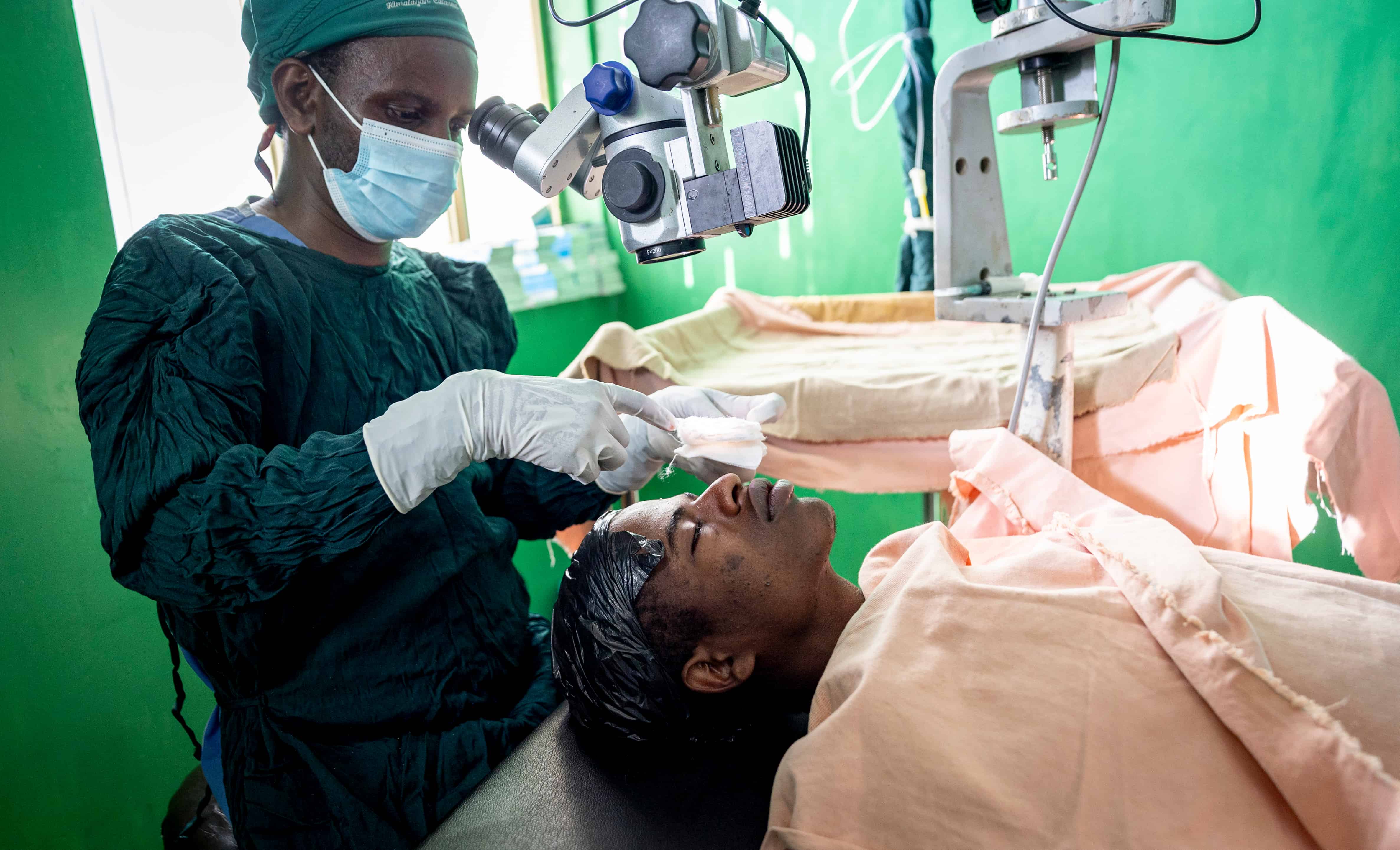 A photo of a surgeon performing an eye operation on a patient. The surgeon is looking through a microscope, and the patient is lying on an operating table.