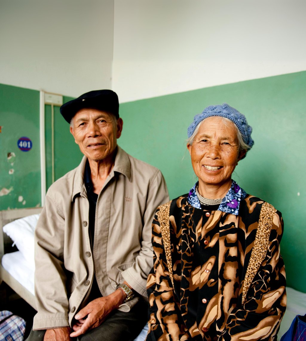 Chinese couple sitting side by side on a hospital bed smiling at the camera