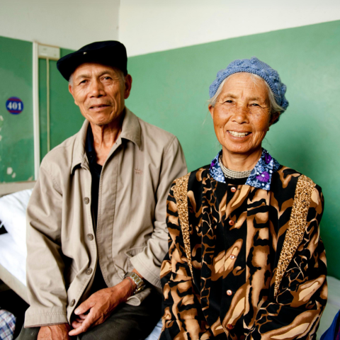 Chinese couple sitting side by side on a hospital bed smiling at the camera