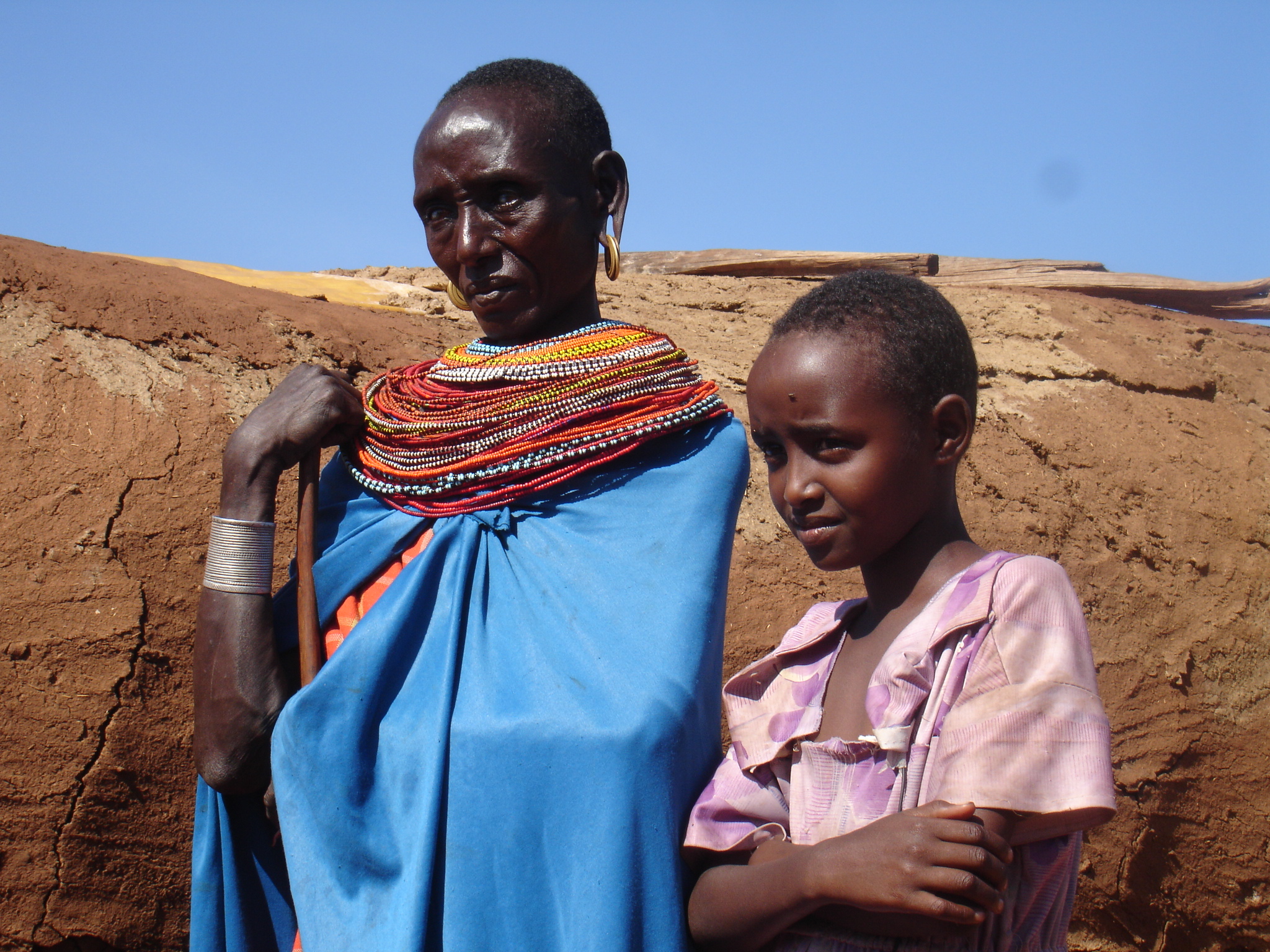 Simila and her mother Rose standing together in the heat, looking off into the distance.